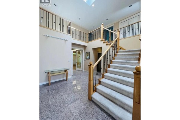 Interior view of the grand foyer showing the staircase and a glass console table. - 8740 Minler Road, Richmond