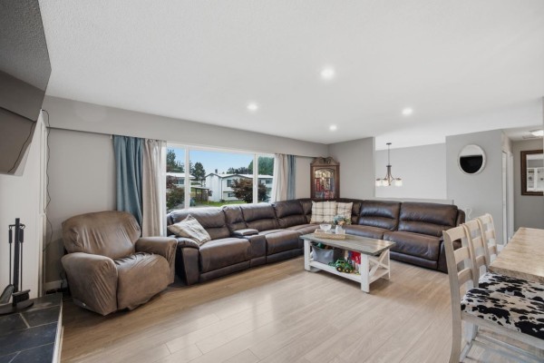 Living room with large brown leather sectional, fireplace, television, and large window. - 8762 Cornwall Crescent, Chilliwack Proper South, Chilliwack