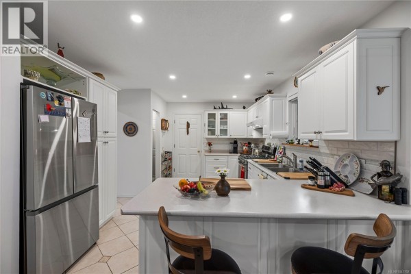 Bright white kitchen with stainless steel appliances, ample cabinet space, and a large island. - 879 Aberdeen Dr, Parksville