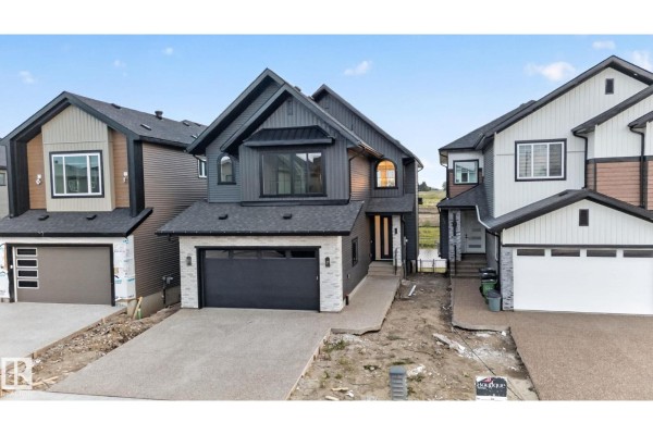 Front exterior of a modern grey house with a black garage door, stone accents, and beige siding. - 8791 Mayday Ln Sw, Edmonton