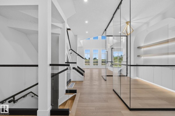 Interior hallway with a modern staircase featuring glass railings and a white wall with built-in shelving. - 8791 Mayday Ln Sw, Edmonton