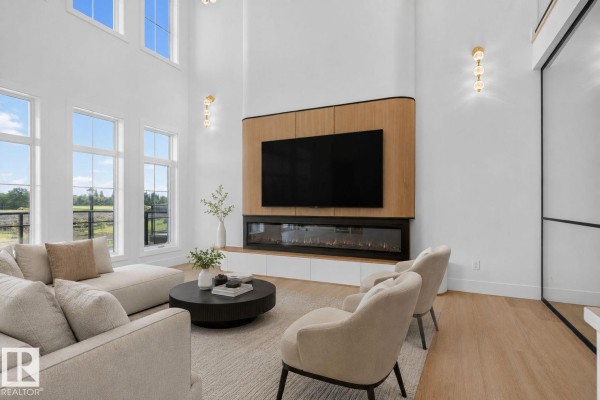 Living room with a large sectional sofa, two armchairs, a round coffee table, and a wall-mounted television above a linear fireplace. - 8791 Mayday Ln Sw, Edmonton