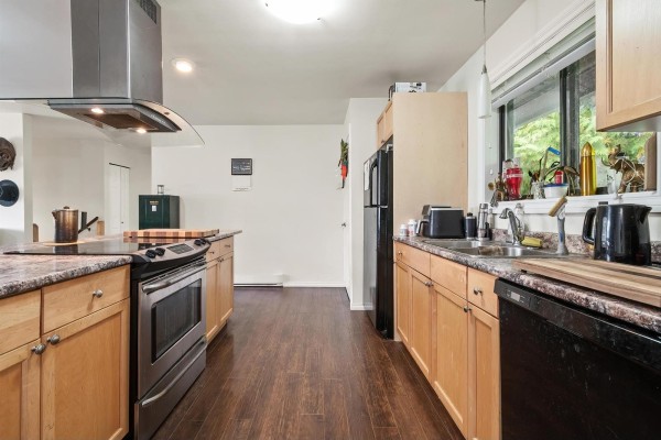 Kitchen counter with a window view, featuring light wood cabinets and black appliances. - 8792 Bellevue Drive, Chilliwack Proper West, Chilliwack