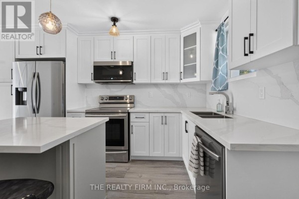 A spacious white kitchen with a stainless steel refrigerator, island, and dining area. - 88 - 1919 Trafalgar Street, London East