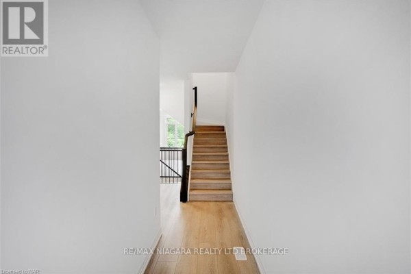 Interior hallway with white walls, light wood flooring, and wooden stairs. - 88 - 4552 Portage Road, Niagara Falls