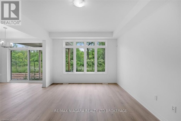 Living area with large window showcasing a wooded backyard and light wood flooring. - 88 - 4552 Portage Road, Niagara Falls
