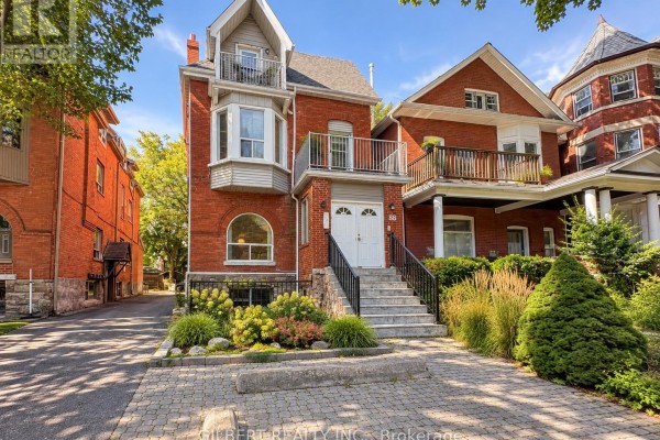 Daytime view of a red brick house with white trim, balconies, bay windows, and a stone base. - 88 Cowan Avenue, Toronto