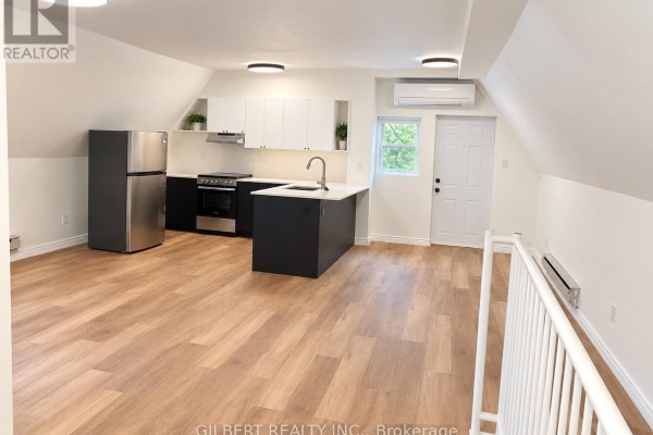 Open concept kitchen and living space with light wood floors, modern white and dark cabinetry, and stainless steel appliances. - 88 Cowan Avenue, Toronto