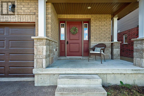 Close-up of the covered front porch entrance with a maroon door, wreath, chair, and stone accents. - 88 Davidson Drive, Stratford