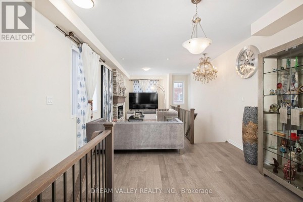 Living room with light wood floors, grey sofa, and a fireplace with a television above. - 88 Jolly Way S, Toronto