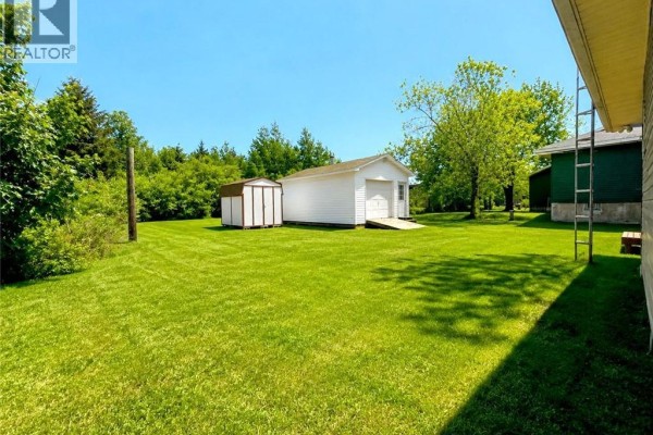 View of a large backyard with a white detached garage and storage shed. - 88 Rue Donat, Pointe Des Robichaud