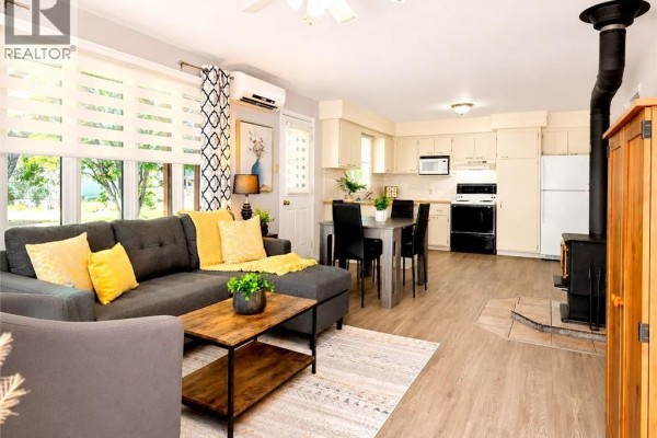 Living room with a grey sectional sofa, coffee table, and kitchen in the background. - 88 Rue Donat, Pointe Des Robichaud