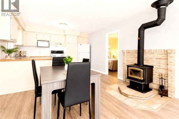 Dining area with a grey table and black chairs, adjacent to the kitchen and a wood stove. - 88 Rue Donat, Pointe Des Robichaud