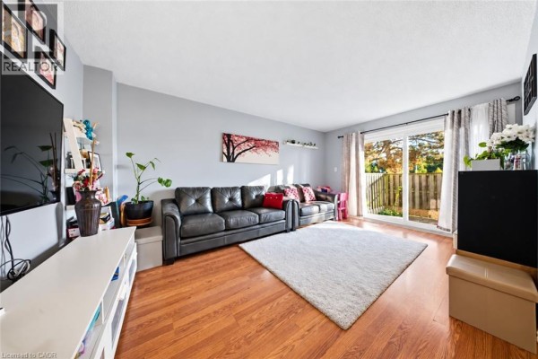 Living room with grey sofa, white shag rug, wood floors, and sliding glass door to backyard. - 880 Limeridge Road E Unit# 59, Hamilton