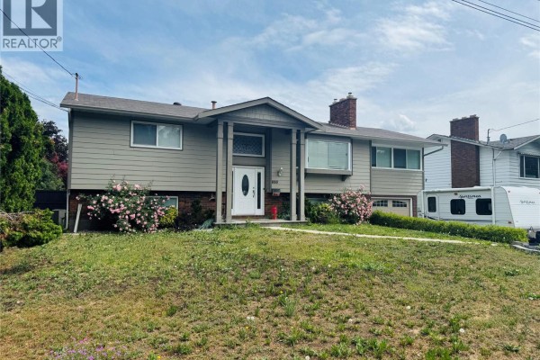 A beige house with a red brick chimney and pink flowering bushes. - 880 Tamarack Drive, Kelowna