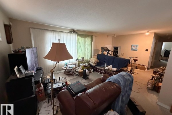 Spacious living area with sofas, a treadmill, television, and doorway leading to another room. - 8816 137 Av Nw, Edmonton