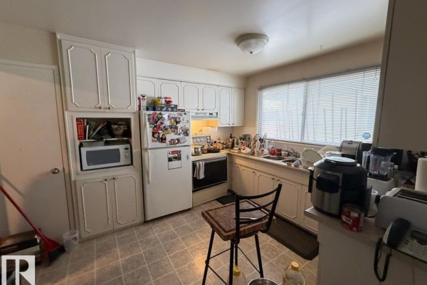 Kitchen with white cabinetry, a refrigerator, oven, microwave, sink, and tiled flooring. - 8816 137 Av Nw, Edmonton