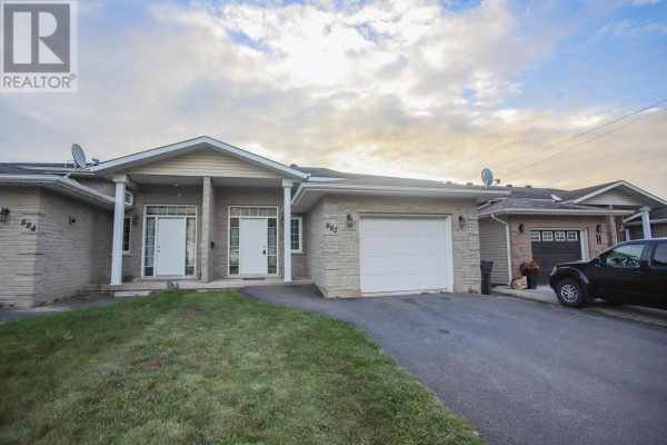 Front view of a bungalow with a concrete driveway and lawn, beige brick and siding. - 882 Pine St, Sault Ste  Marie
