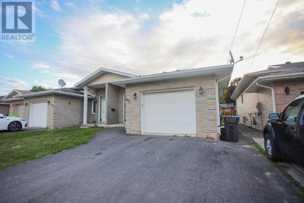 Side exterior view of a bungalow with a concrete driveway, beige brick and siding, and white garage door. - 882 Pine St, Sault Ste  Marie