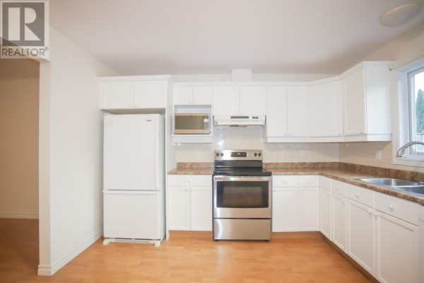 Kitchen with white cabinets, stainless steel appliances including a refrigerator, oven, and microwave, and laminate flooring. - 882 Pine St, Sault Ste  Marie