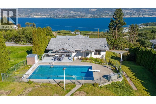 Aerial view of a house with a swimming pool, deck, and large blue lake in the background. - 8820 Happy Valley Road, Summerland