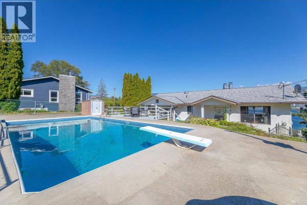 Swimming pool with a diving board in front of a house with a distant lake view. - 8820 Happy Valley Road, Summerland