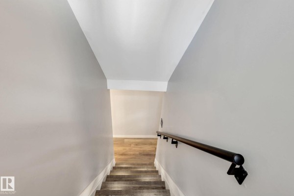 View looking down a staircase with light grey walls and a black handrail. - 8823-8825 95 St Nw, Edmonton