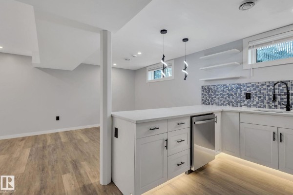Modern kitchen with white cabinets, grey tiled backsplash, and stainless steel appliances. - 8823-8825 95 St Nw, Edmonton