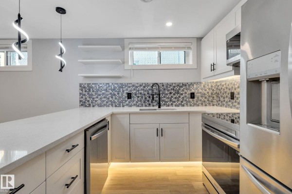 U-shaped kitchen with white countertops, grey tiled backsplash, and stainless steel appliances. - 8823-8825 95 St Nw, Edmonton