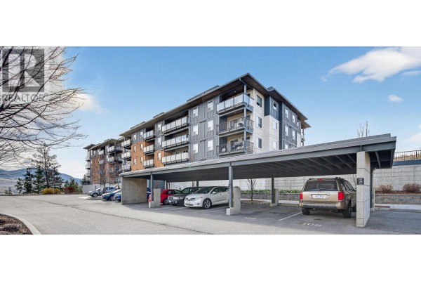 Covered parking area with several vehicles and the apartment building in the background - 883 Academy Way Unit# 116, Kelowna