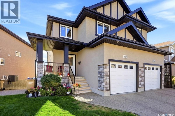 Front view of a beige house with stone accents, dark trim, and a double garage. - 8837 Kestral Drive, Regina