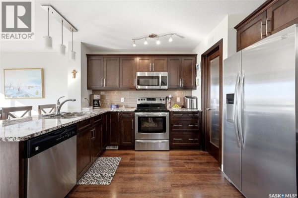 Kitchen with dark wood cabinets, granite countertops, stainless steel appliances, and hardwood floors. - 8837 Kestral Drive, Regina