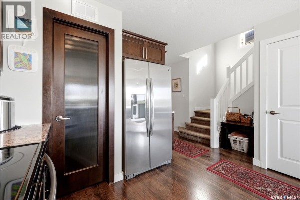Kitchen area with a stainless steel refrigerator, dark wood cabinets, and stairs leading up. - 8837 Kestral Drive, Regina