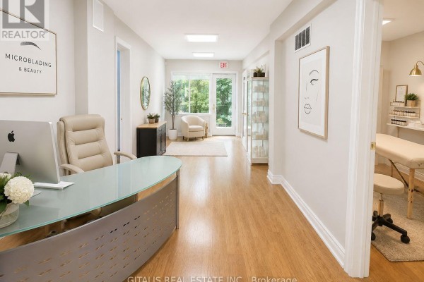 Reception area with light wood floors, desk, and treatment room access. - 884 College Street, Toronto