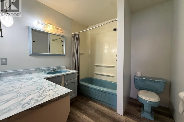 Blue bathtub and toilet in a bathroom with a vanity and marble countertop. - 8845 Central St, Port Hardy