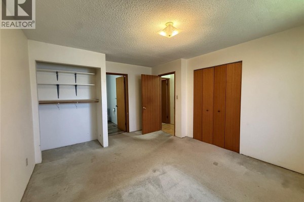 Bedroom with carpeted floor, wooden closet doors, and open closet shelves. - 8845 Central St, Port Hardy
