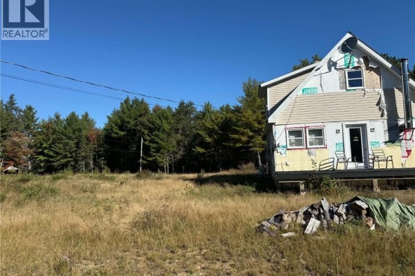 House exterior with tall pine trees and a clear blue sky, showing the front entrance. - 886 Cains River Road, Cains River