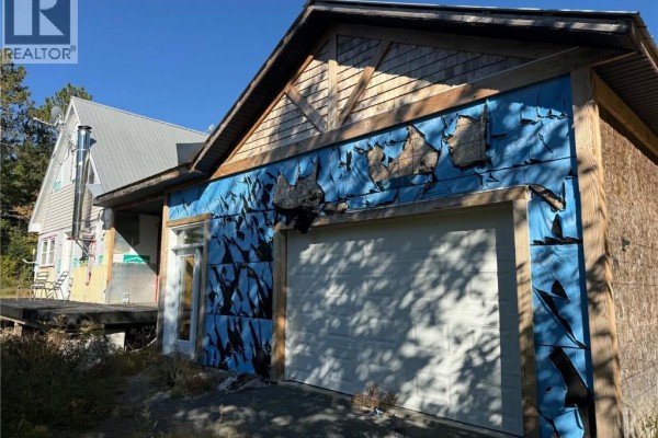 Close-up of the garage door and partially removed blue siding on the right side of the house. - 886 Cains River Road, Cains River