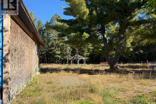 View of the backyard with a wooden gazebo and mature trees, seen from the side of the house. - 886 Cains River Road, Cains River
