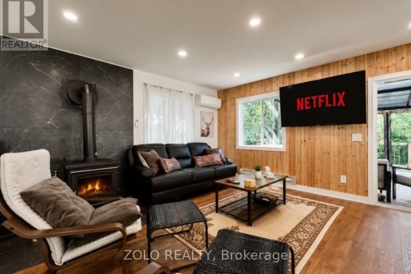 Living room with black sofa, wood-paneled accent wall, and wood-burning stove. - 886 Monck Road, Kawartha Lakes