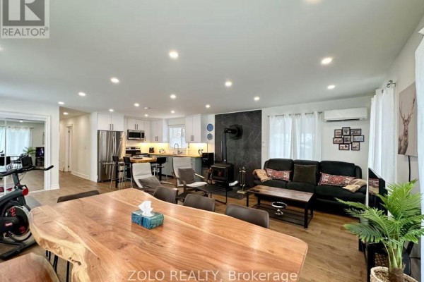 Open concept living, dining, and kitchen area with a large wooden dining table. - 886 Monck Road, Kawartha Lakes