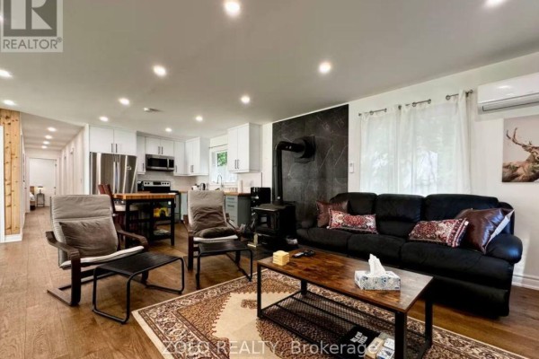 View of the open-concept living area showing the kitchen, dining table, and sofa. - 886 Monck Road, Kawartha Lakes