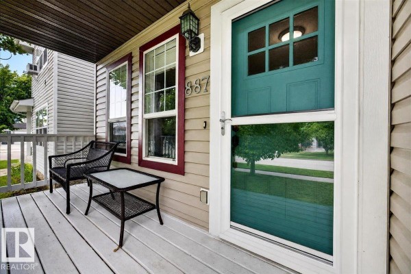 Exterior view of the front entrance and side of a house with beige siding and maroon trim, featuring a green front door. - 887 Oakland Bv, Devon