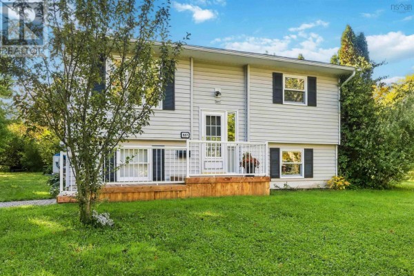 Front exterior of a light grey house with a wooden deck and white railings, surrounded by green grass. - 887 Richard Street, Kentville