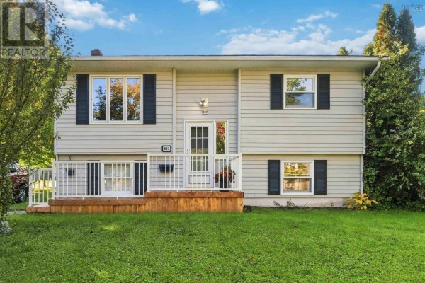 Front elevation of the light grey house with dark shutters and windows, set against a backdrop of trees. - 887 Richard Street, Kentville
