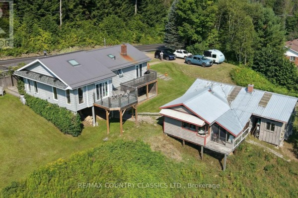Aerial view of two light grey houses on a grassy slope surrounded by trees. - 888 Wilno South Road S, Madawaska Valley