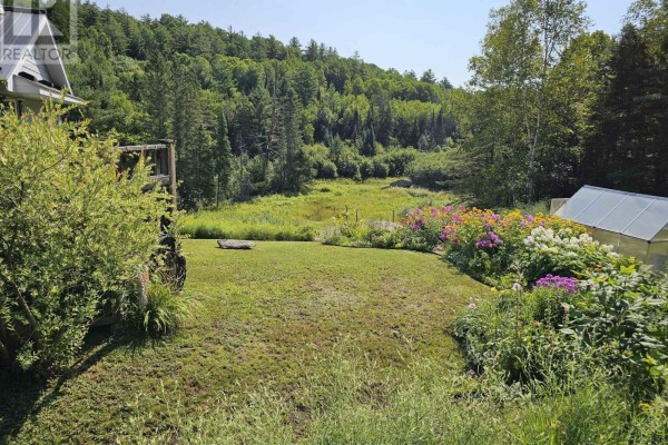 View of a backyard with a lawn, flower beds, a greenhouse, and a wooded area. - 888 Wilno South Road S, Madawaska Valley