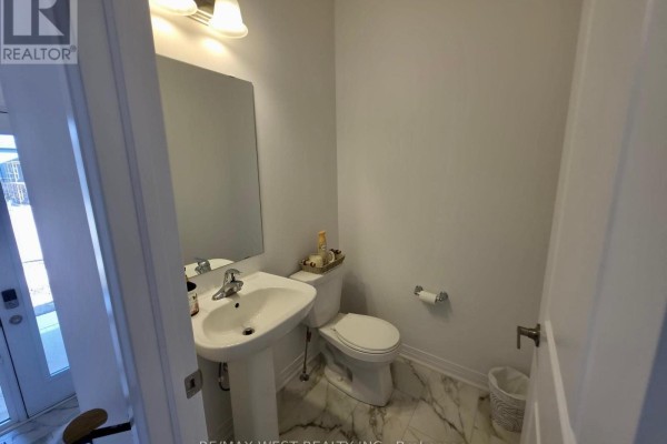 Powder room with a pedestal sink, toilet, white vanity, and marble-patterned floor tiles. - 889 Douro Street, Stratford