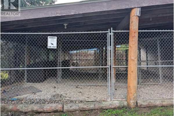 Chain-link fence enclosing outdoor dog kennels with gravel and wood chip flooring. - 8893 Holding Road, Adams Lake