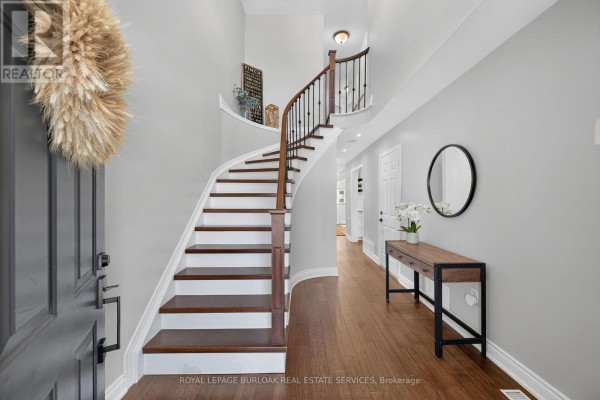 Interior foyer with a curved wooden staircase, grey walls, and hardwood floors. - 89 - 4055 Forest Run Avenue, Burlington